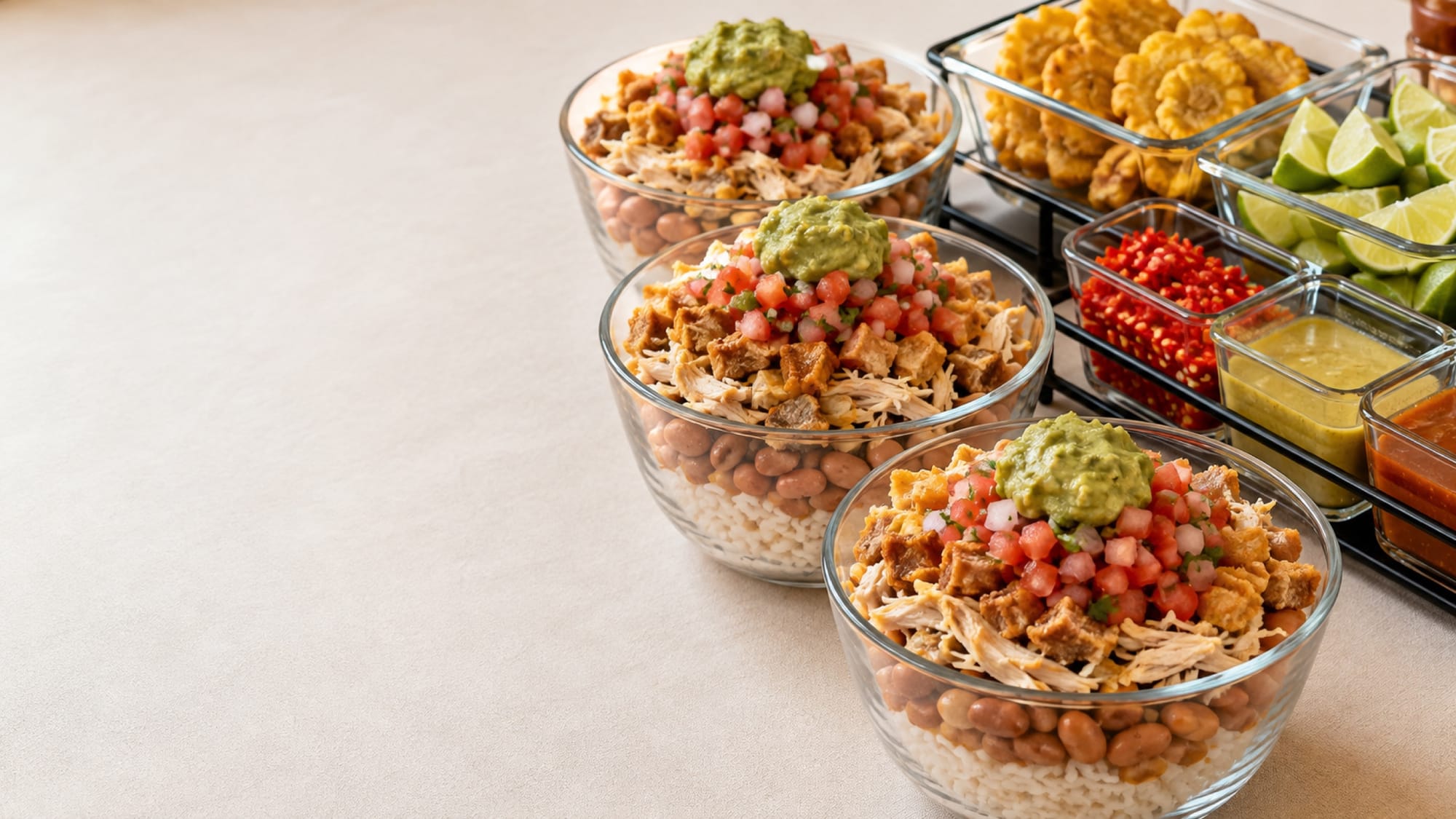 Tres bowls de chifrijo armados en capas junto a bandejas de tostones, limón en gajos, chilito y salsas para combinar